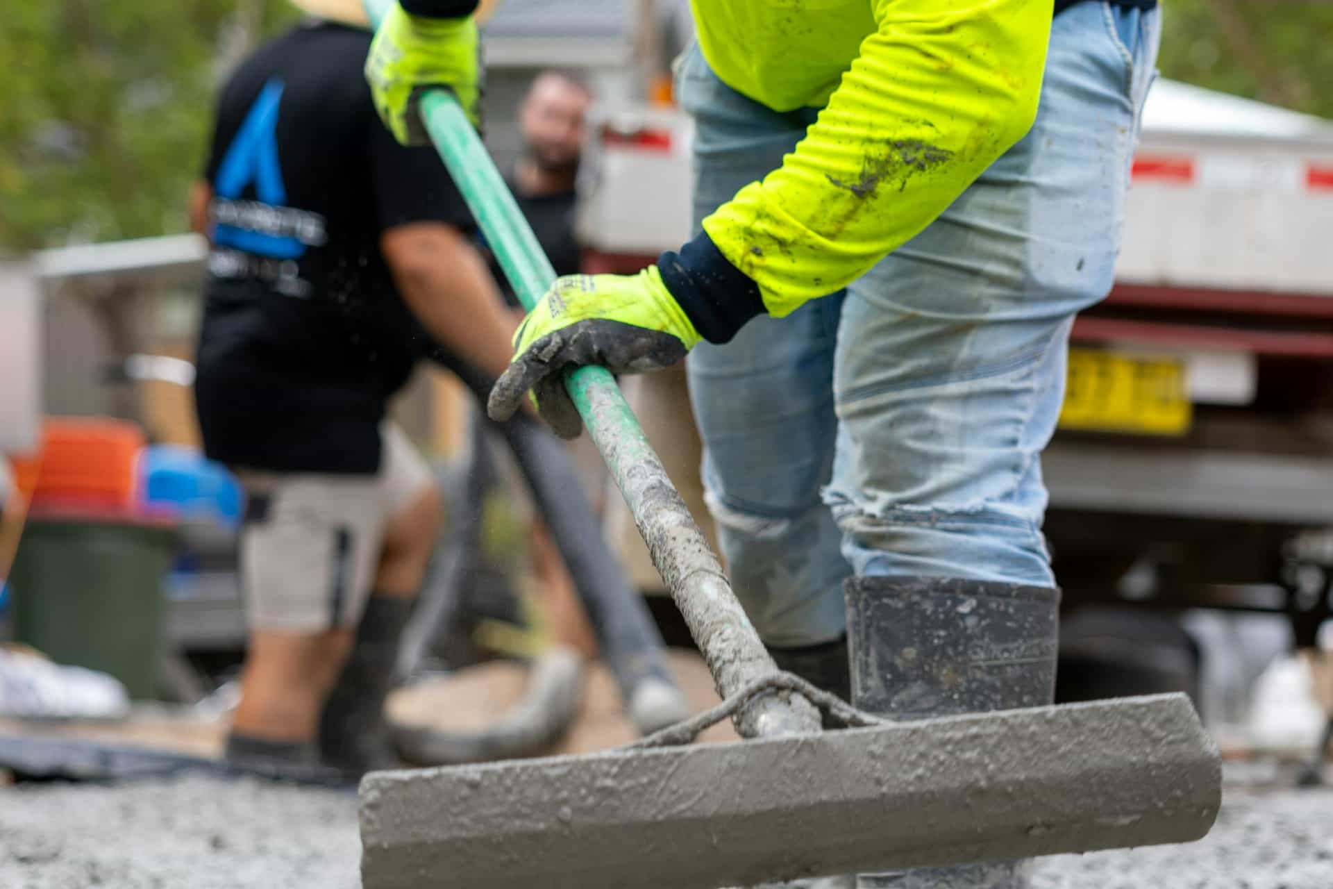 Concrete contractor in high-visibility gear finishing a fresh slab