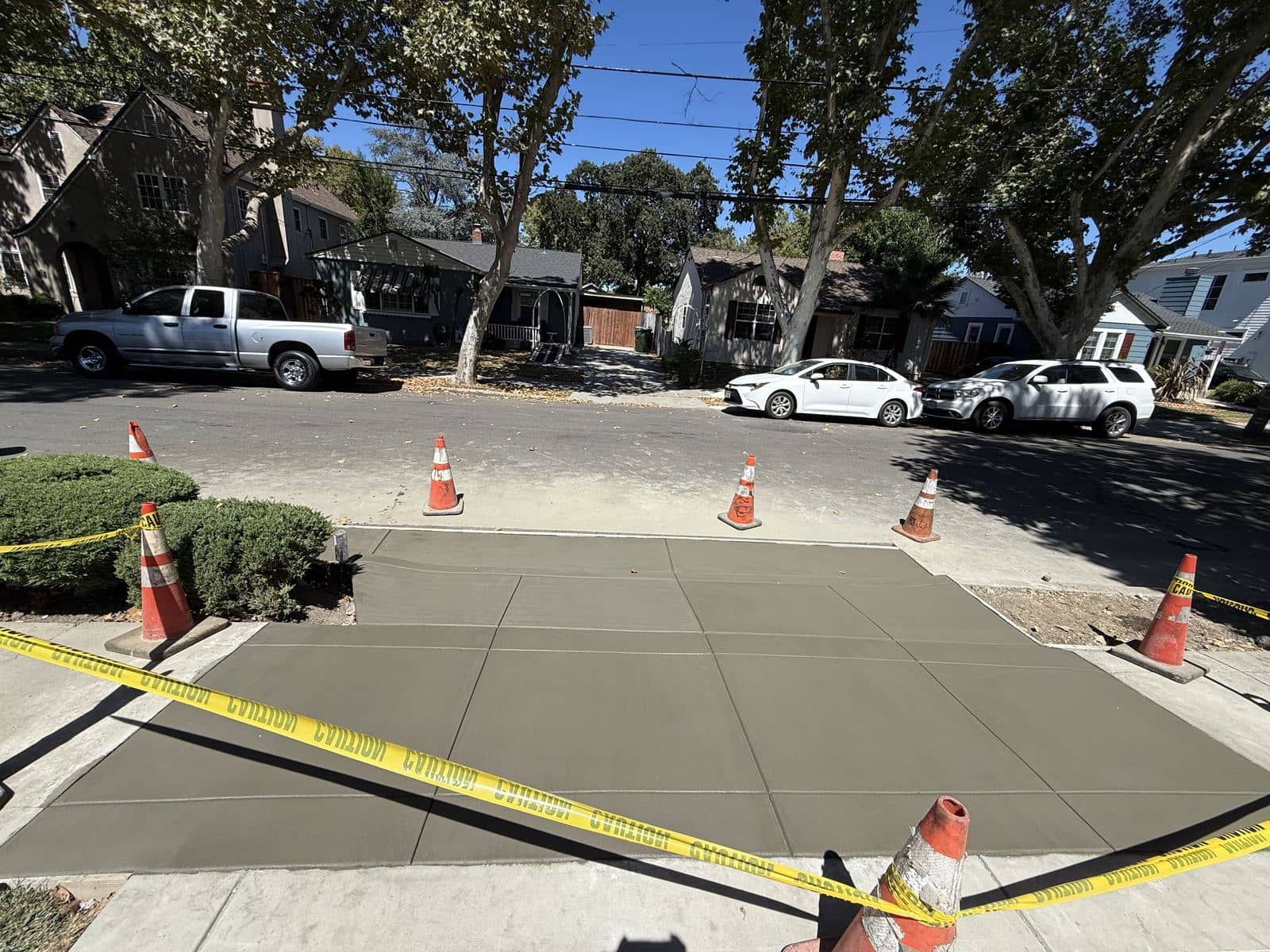 Street view of a new concrete driveway apron curing with safety cones in place