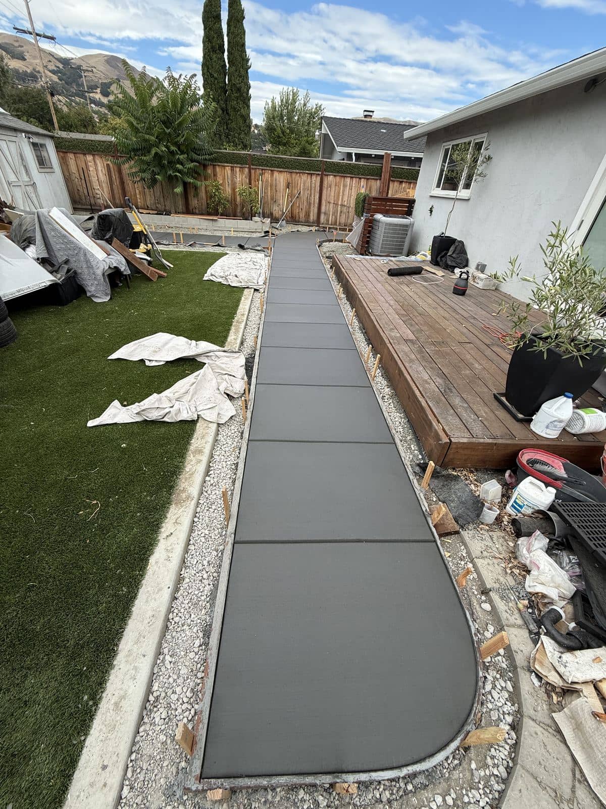 Long concrete walkway poured between a new artificial turf lawn and a wood deck