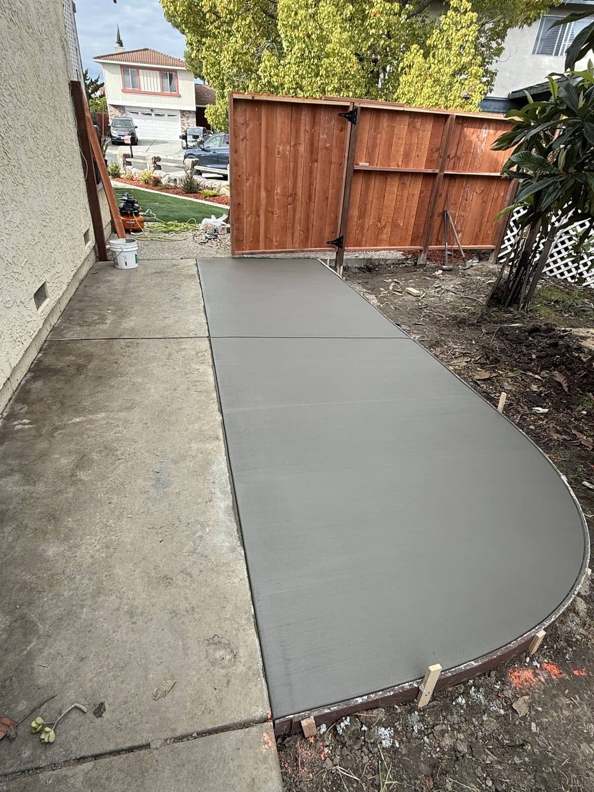 Freshly poured curved concrete walkway extending along a side yard fence