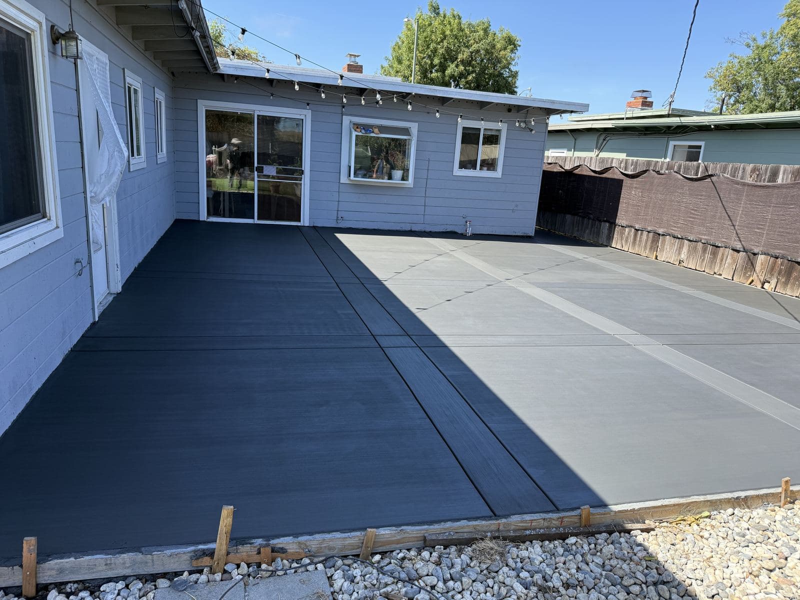 Large finished backyard patio with a two-tone broom finish behind a ranch-style home