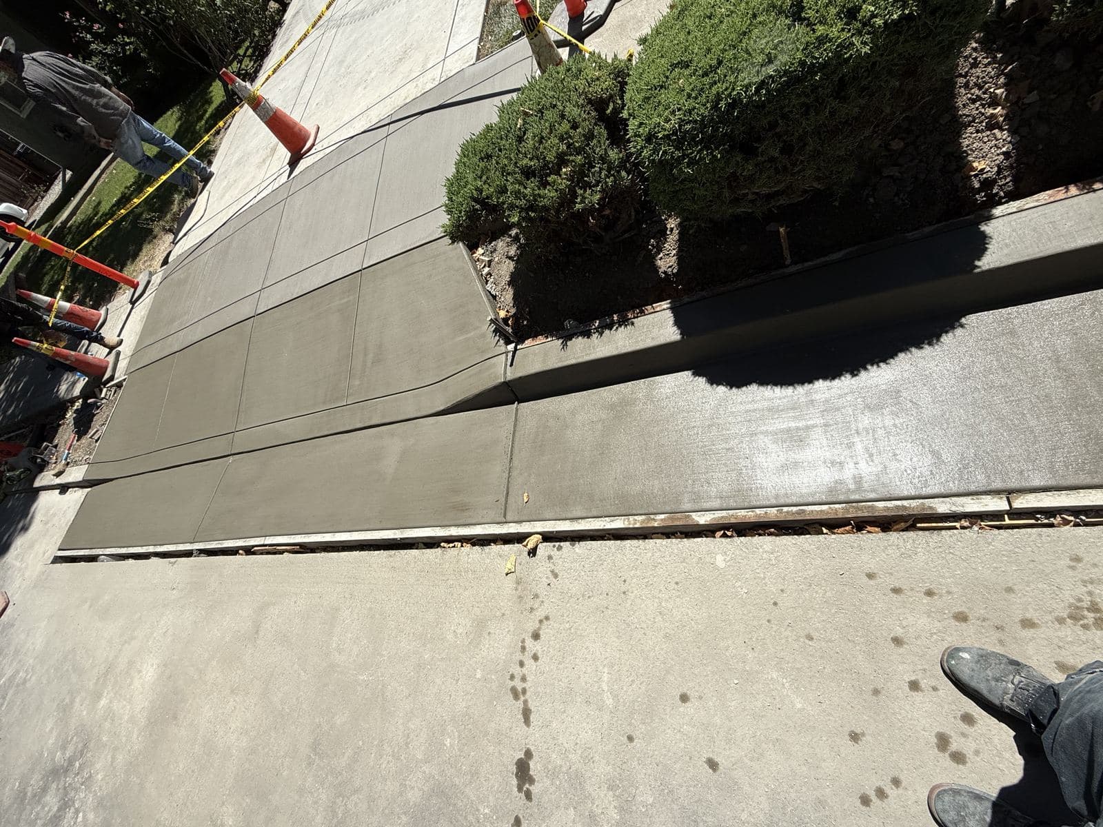 Overhead view of a freshly finished concrete driveway apron next to a curb ramp