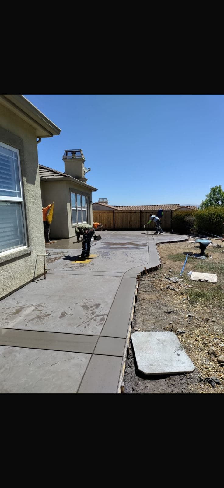Concrete crew hand-finishing a curved backyard patio pour on a sunny day