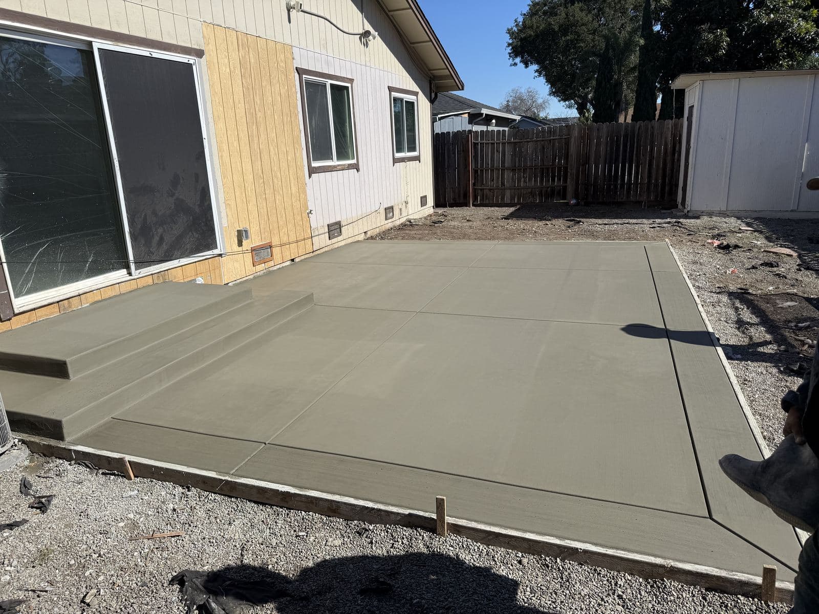 Freshly poured concrete patio and steps still showing wet formwork against a San Jose home