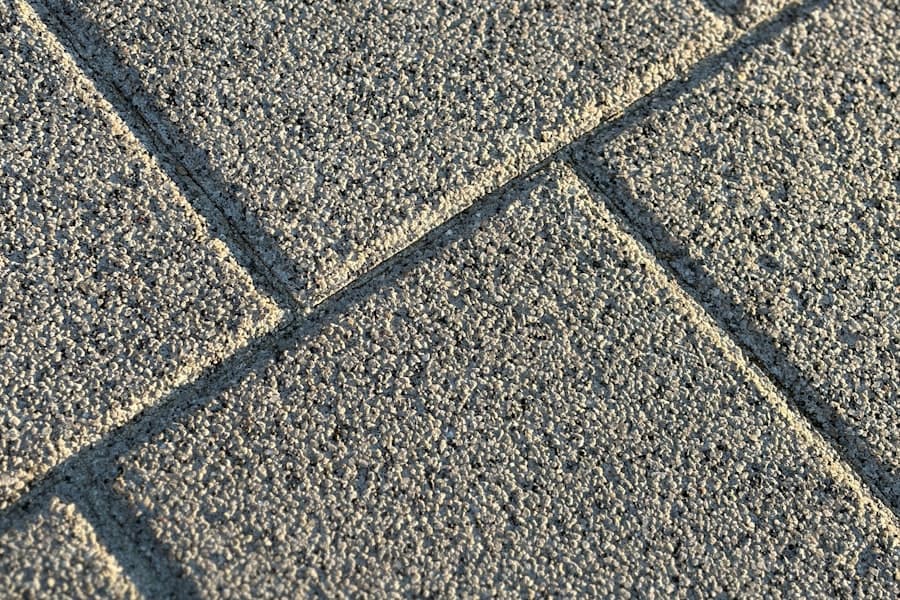 Sunlit close-up of square decorative concrete pavers with a textured finish