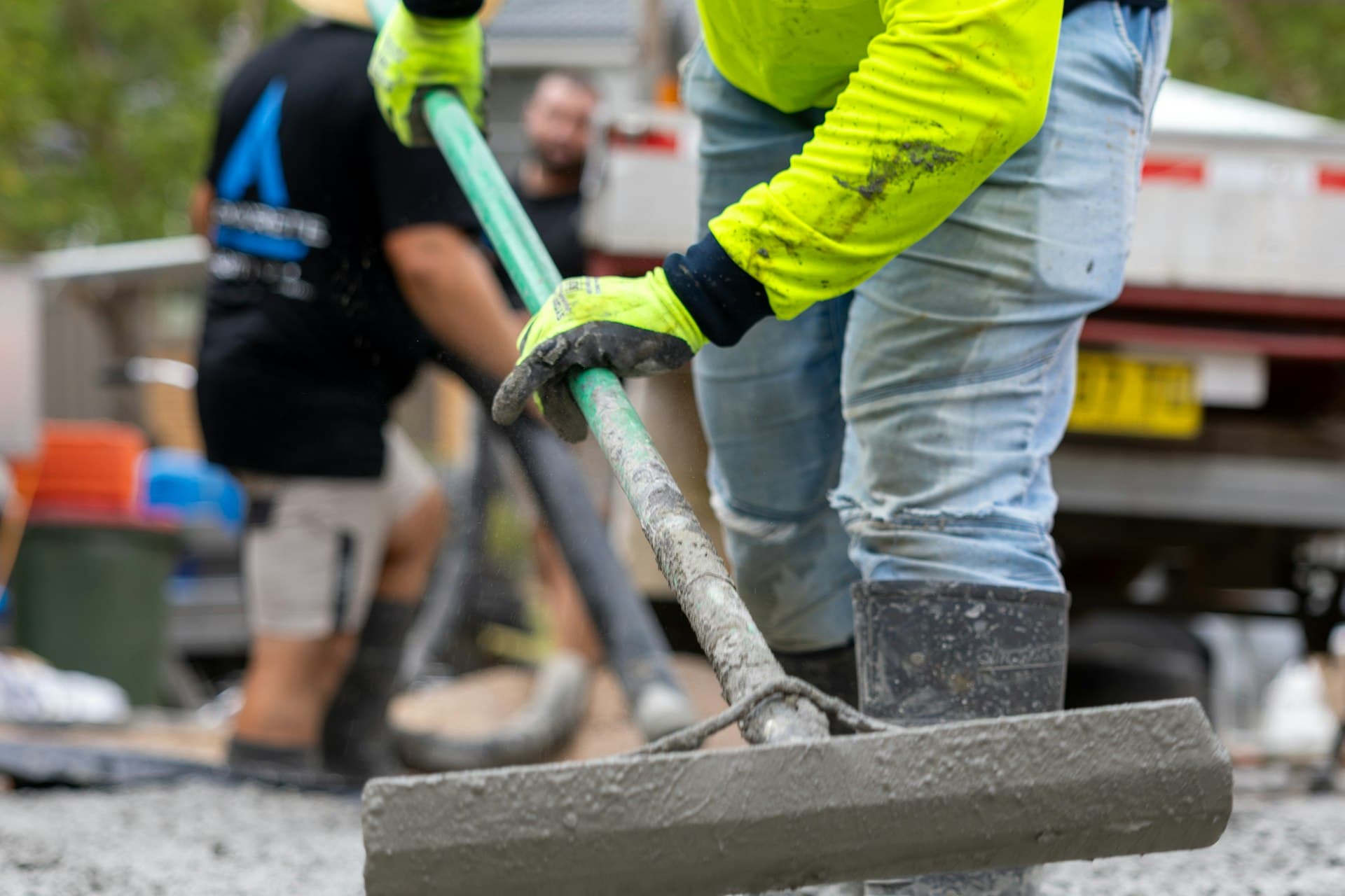 Concrete contractor in high-visibility gear finishing a fresh slab